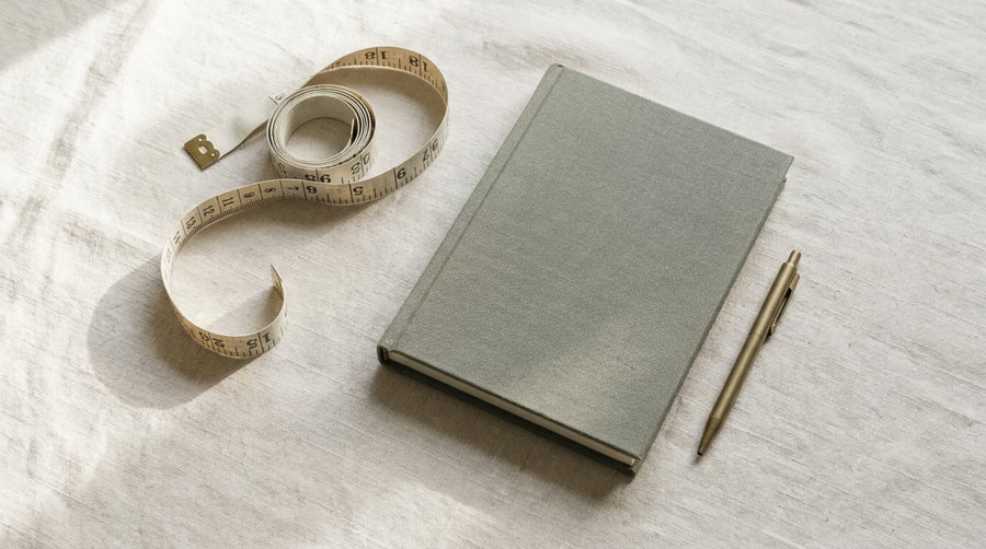 Maßband und Notizbuch auf Leinentuch, Symbol für Gewichtserhalt nach dem Absetzen der Abnehmspritze