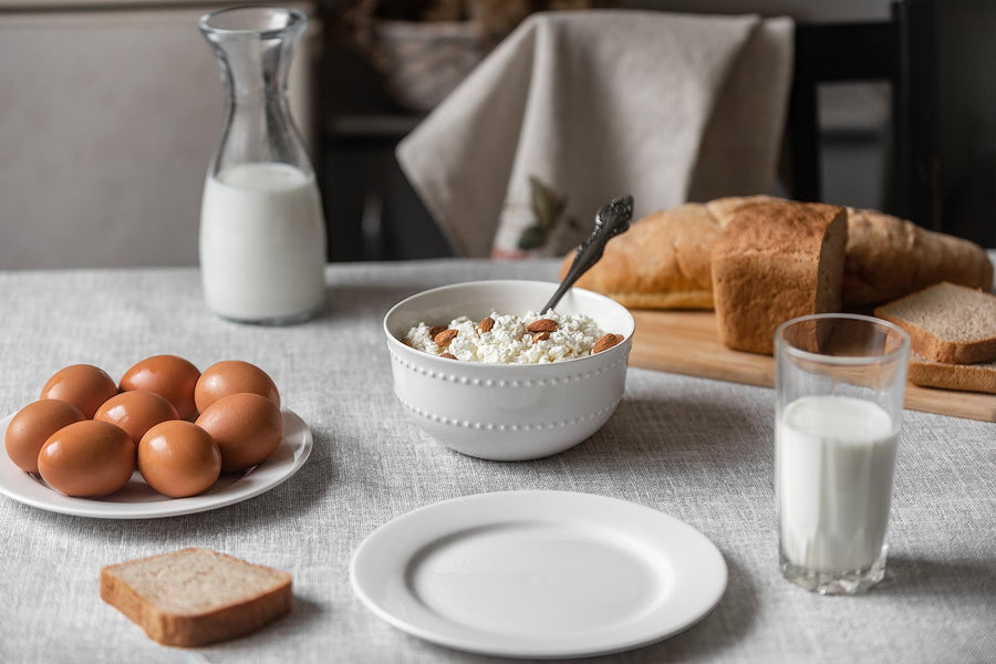 Schale mit Cottage Cheese und Mandeln, daneben ein Teller mit braunen Eiern, Milch und Brot auf einem hellen Leinentischtuch
